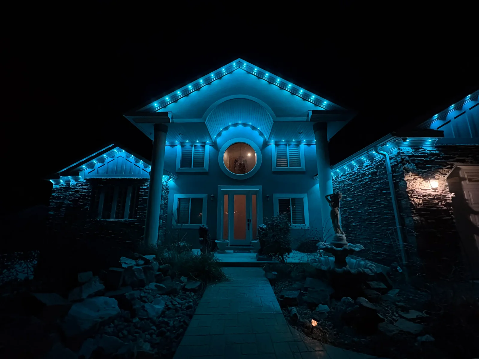 Modern home with blue LED accent lighting on roofline, gables, and architectural features at night