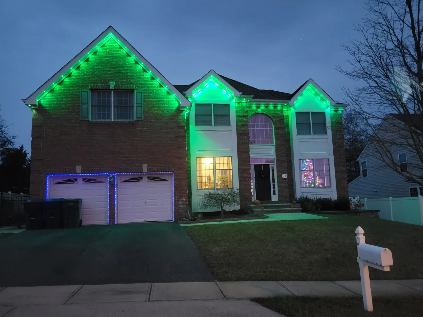 Green LED accent lighting on brick home rooflines and gables with blue garage door lighting at dusk