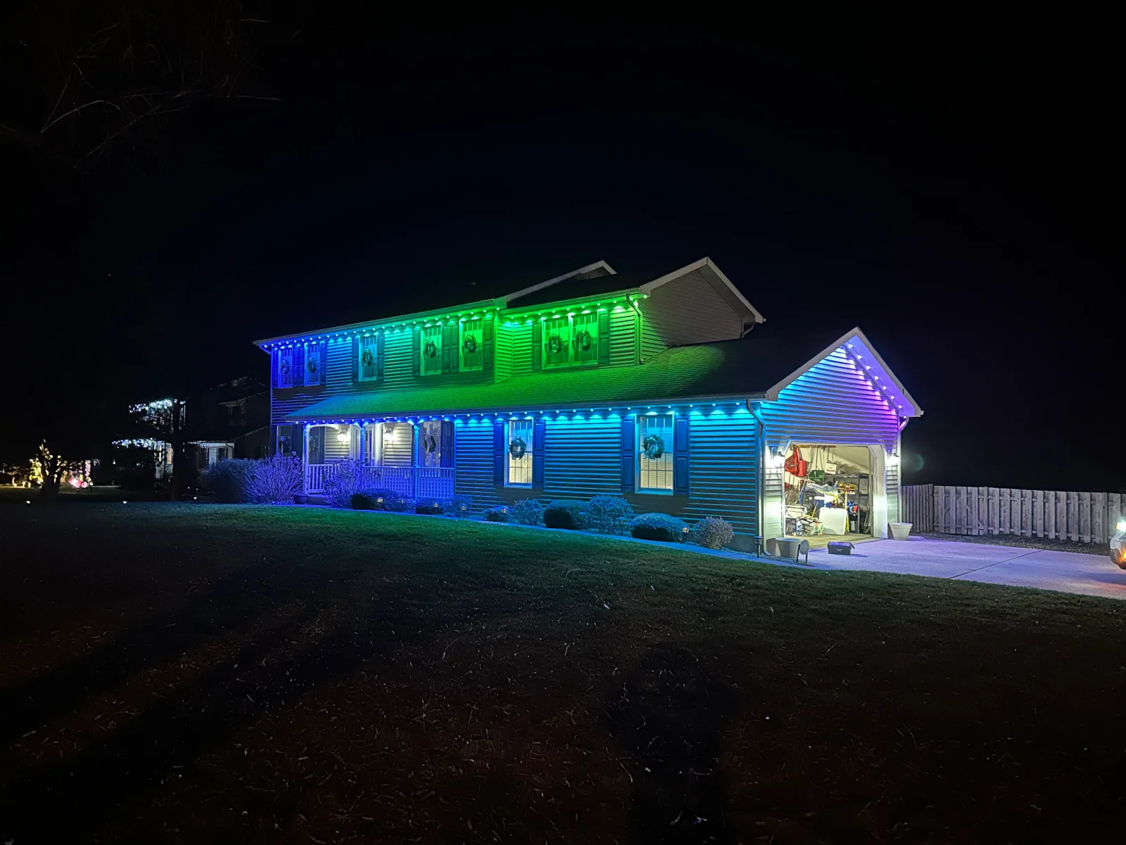 Two-story home with blue and green LED accent lighting on siding and roofline at night
