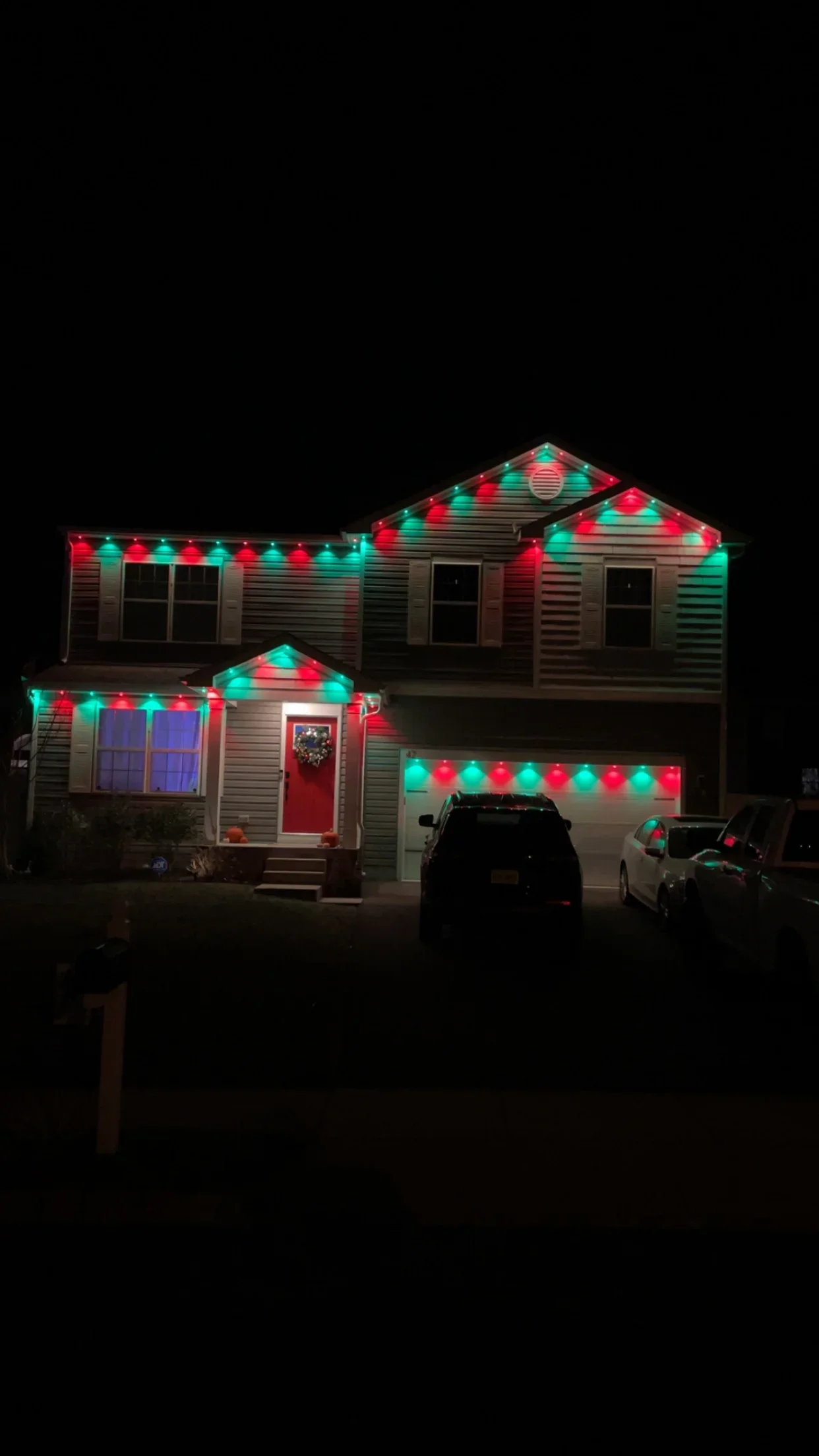 Two-story home with red and green LED holiday lights installed on rooflines, gables, and garage door
