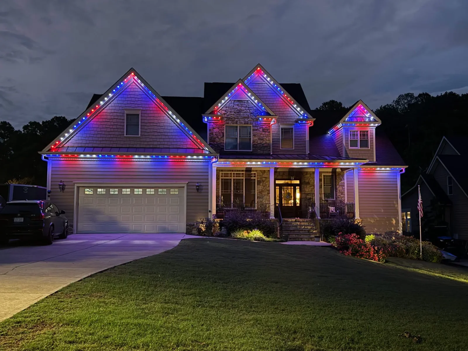 Two-story home with RGB LED accent lighting on roofline, gables, and fascia in blue and red colors
