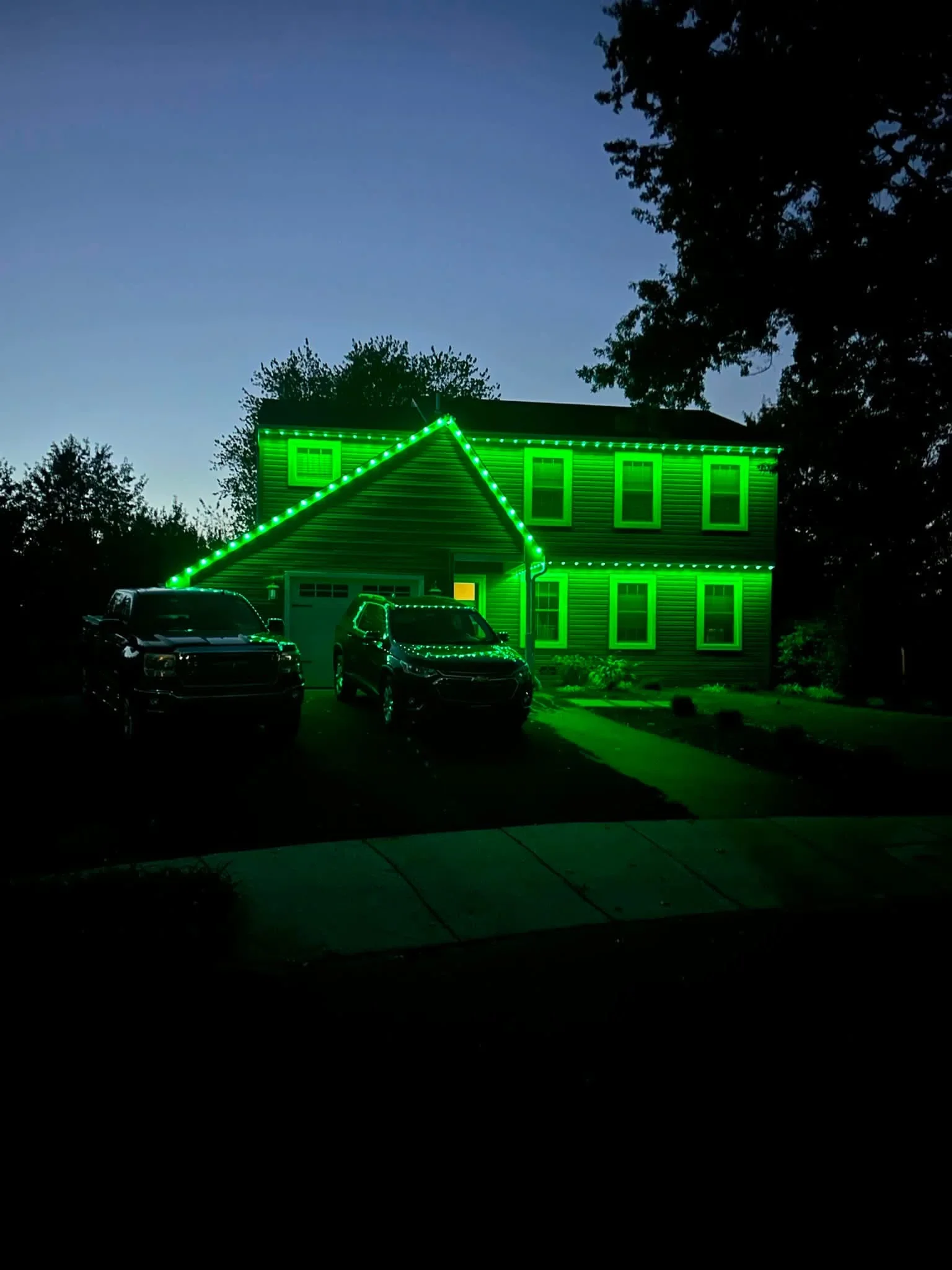 Two-story home with bright green LED rope lights outlining roofline, windows, and garage at night