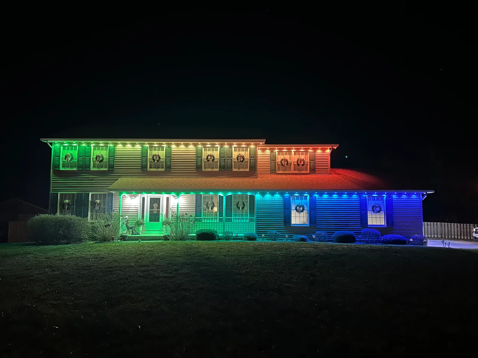Two-story home with full-facade LED lighting in green, blue, and red color zones at night