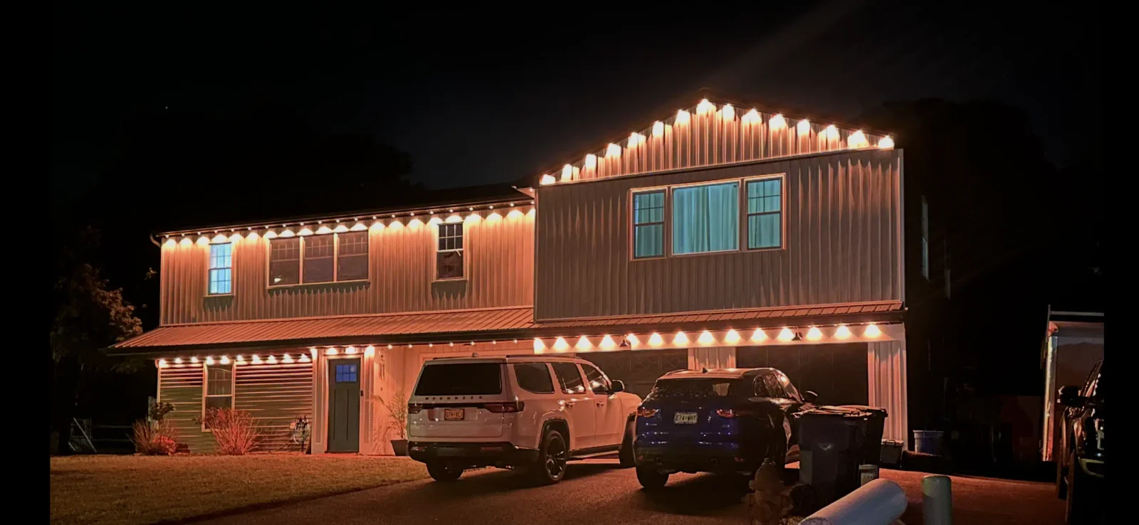 Two-story home with warm white LED uplighting on roofline, soffit lights, and garage accent lighting at night