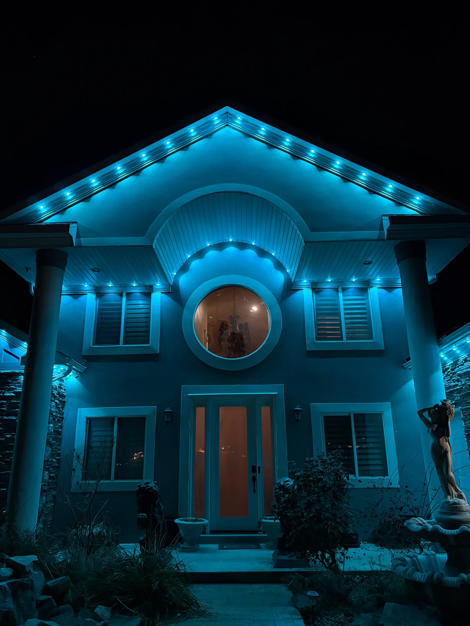 Home facade with blue LED rope lighting on roofline and circular architectural accent light