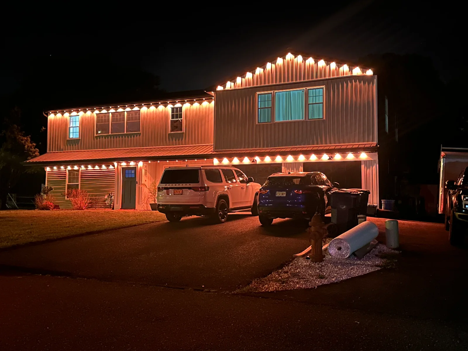 Metal-sided home with warm LED accent lighting along roofline and garage, illuminated at night