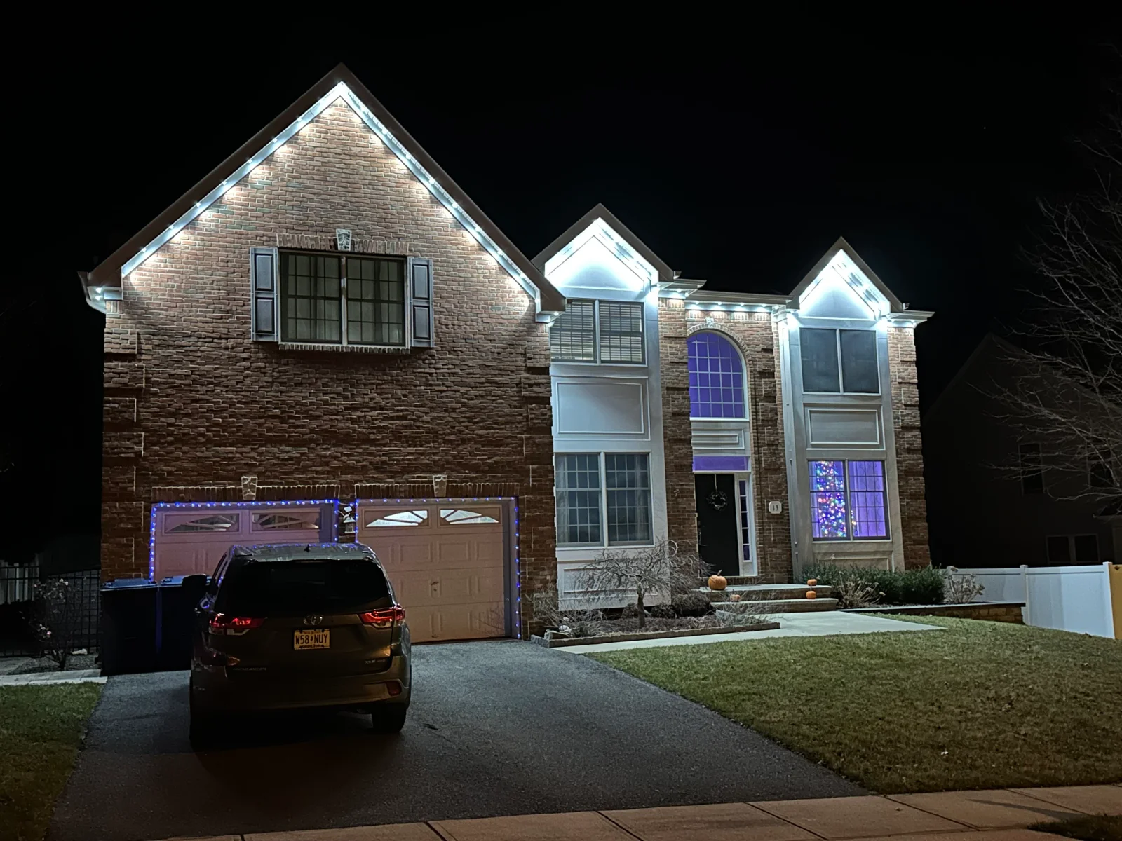 Brick home at night with LED accent lighting on rooflines, garage doors, and architectural features